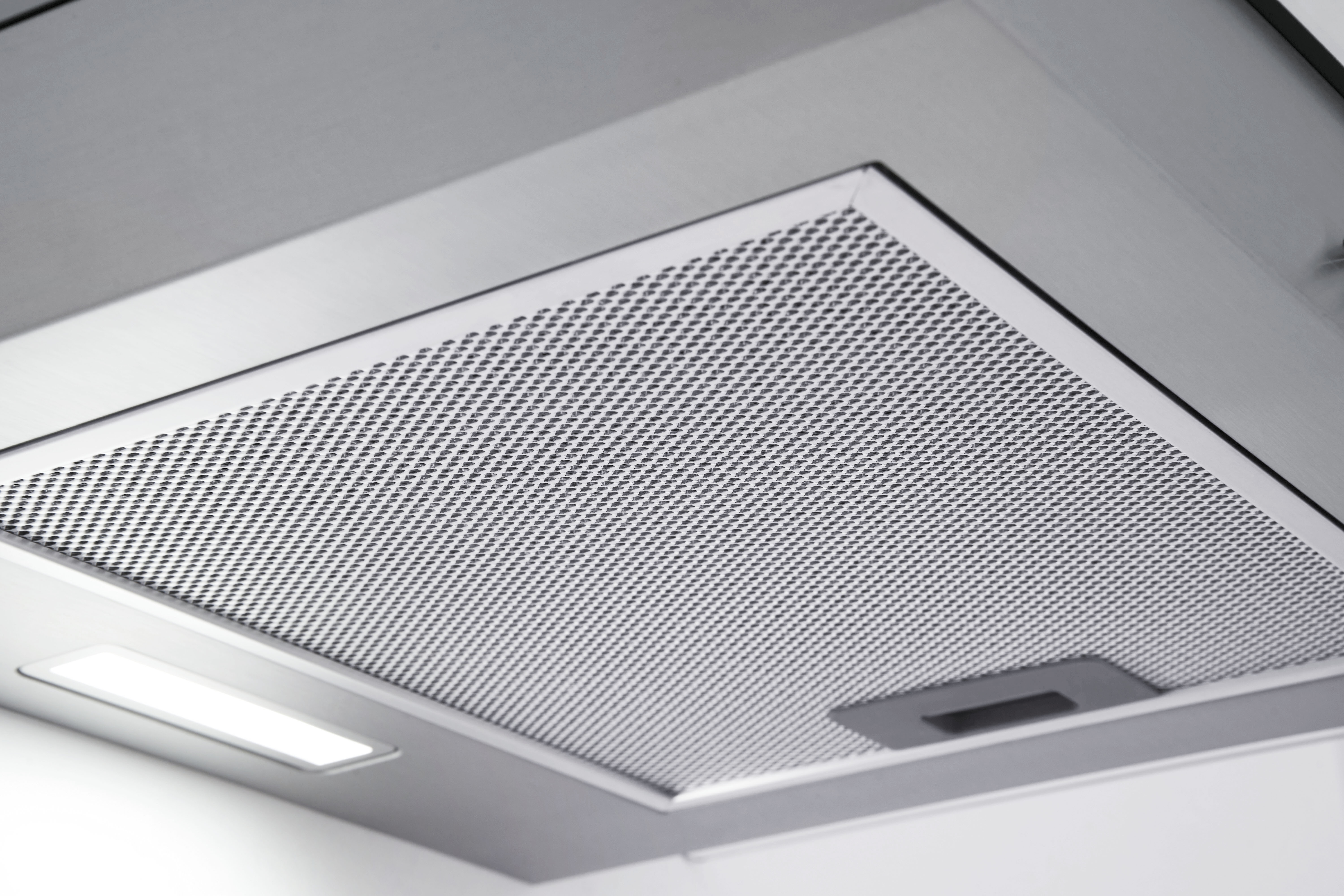 A close-up of a silver range hood filter with a light.