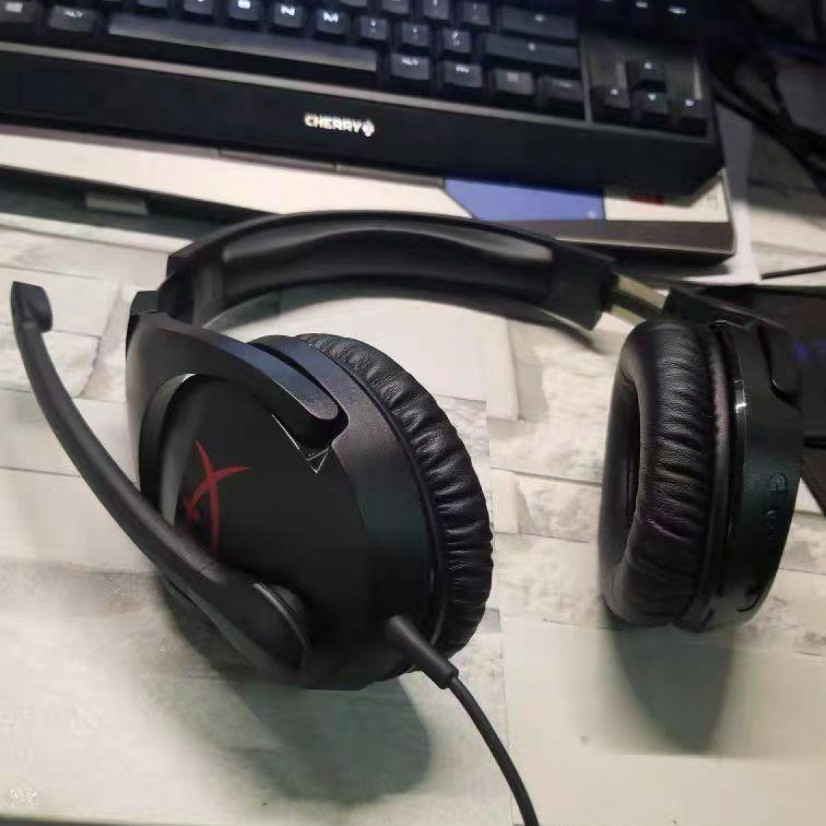 Auriculares para juegos negros con micrófono sobre un escritorio. Los auriculares tienen un logotipo X rojo.