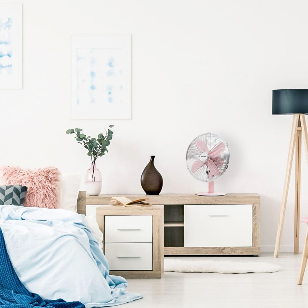Una camera da letto con un ventilatore rosa su un mobile di legno. C'è un letto con una coperta blu e cuscini.
