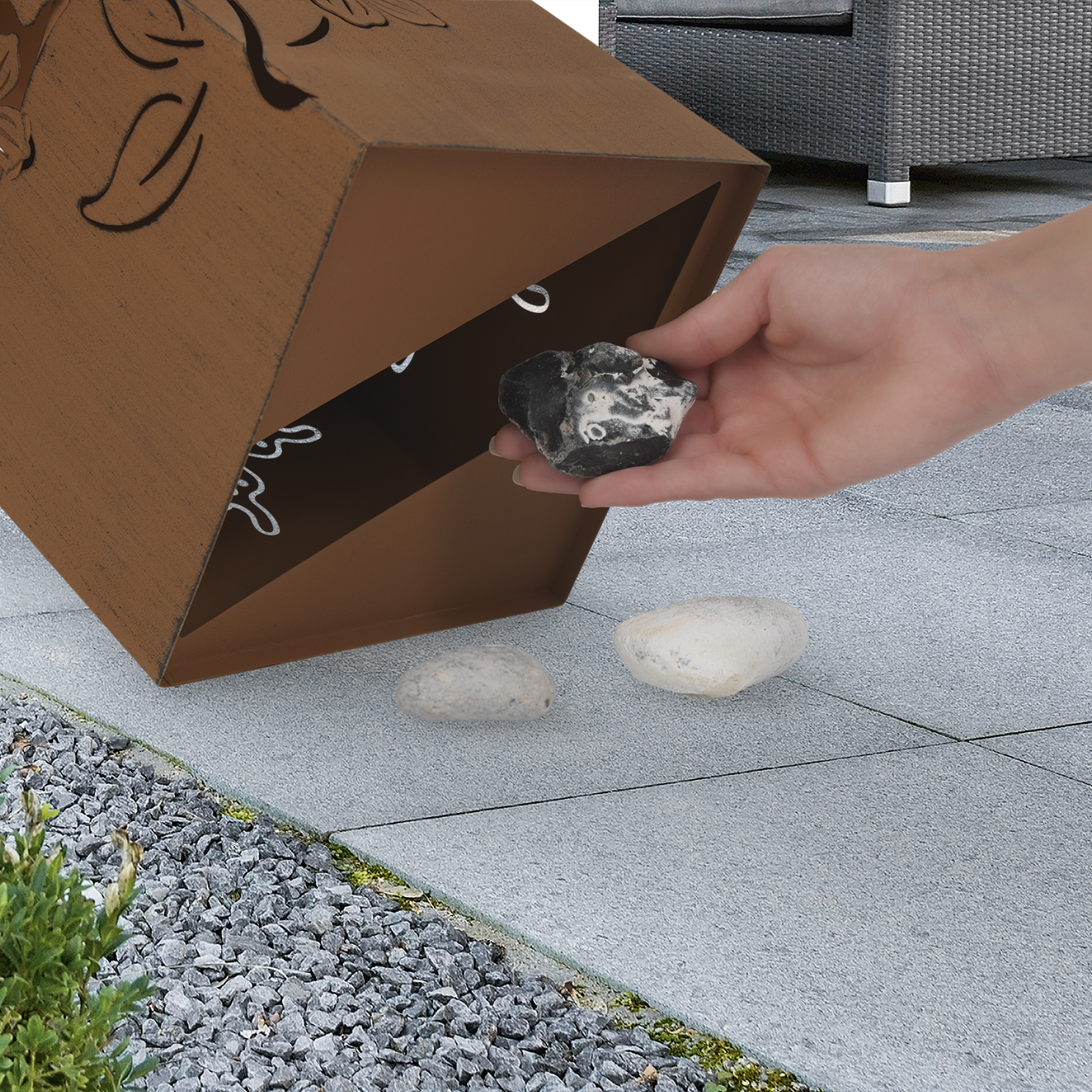 Eine Hand legt einen schwarzen Stein in eine Kiste. Andere Steine ​​liegen auf dem Betonboden verstreut.