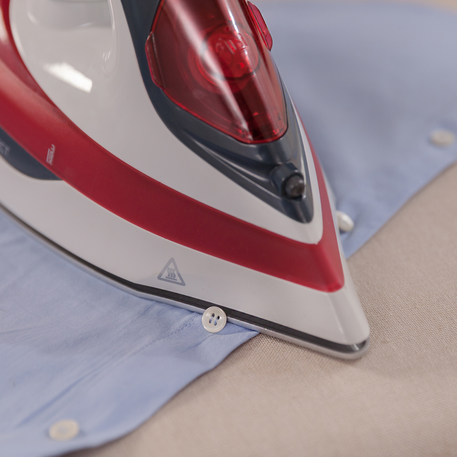 Plancha sobre camisa azul. Plancha roja y blanca. La plancha está sobre un botón. Vista de cerca.