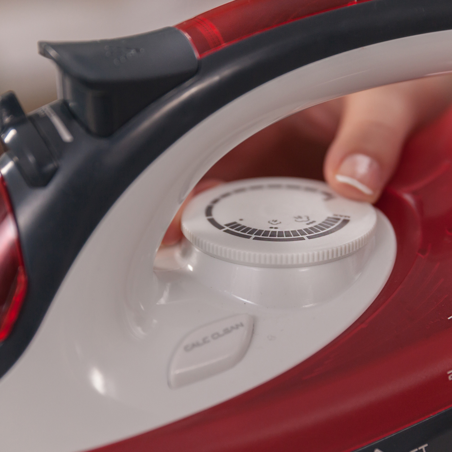 Primer plano de una plancha roja y negra, mano girando un dial blanco con marcas.
