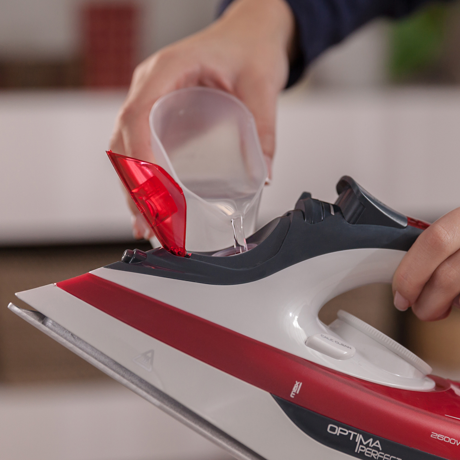 Una persona vierte agua en una plancha roja y blanca con una taza medidora transparente.