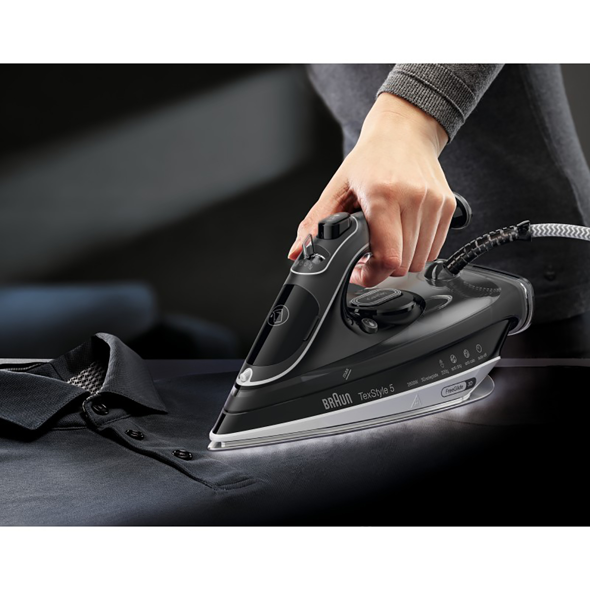 Osoba prasująca czarną koszulę czarno-szarym żelazkiem. Widoczna marka Braun.