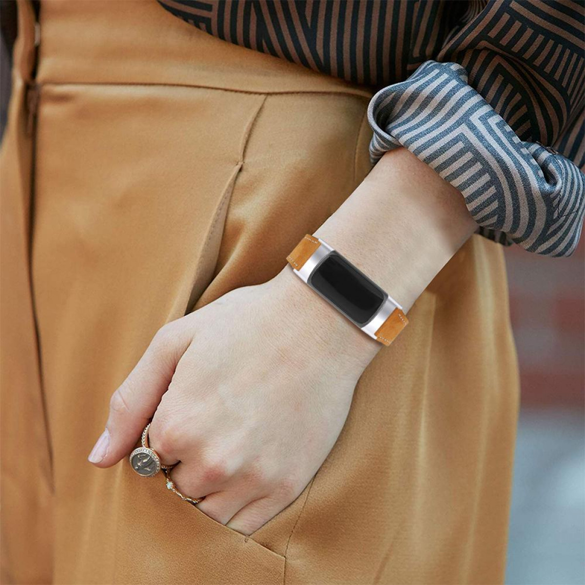 Polso di una persona con un fitness tracker. Cinturino in pelle, schermo nero. Anello e abiti color cuoio.
