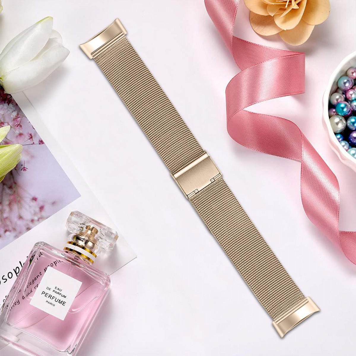 Goldenes Mesh-Armband mit Verschluss, liegt auf einer weißen Oberfläche mit Parfüm und Perlen.