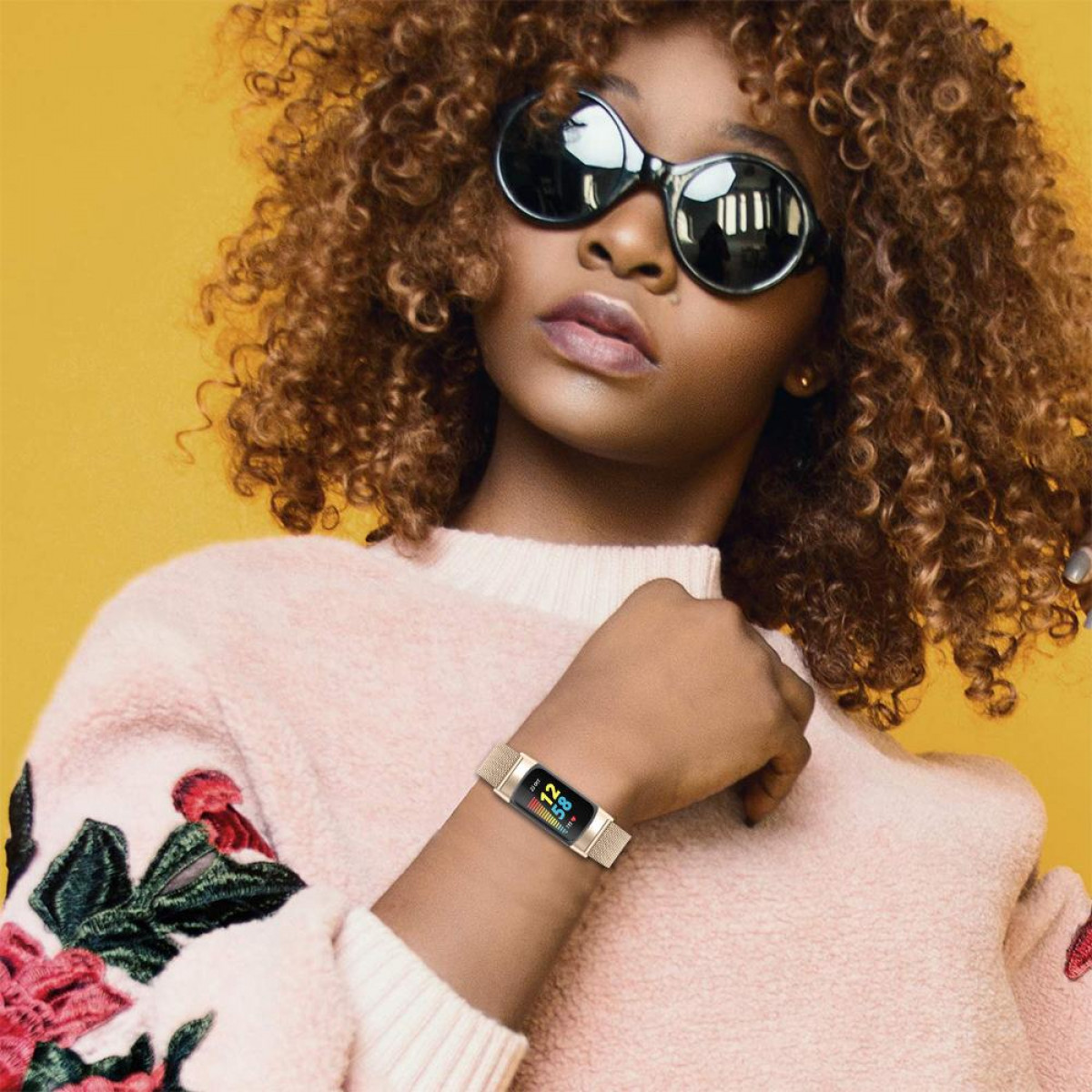 Eine Frau mit Sonnenbrille und pinkem Pullover. Sie hat eine goldene Uhr am Handgelenk.