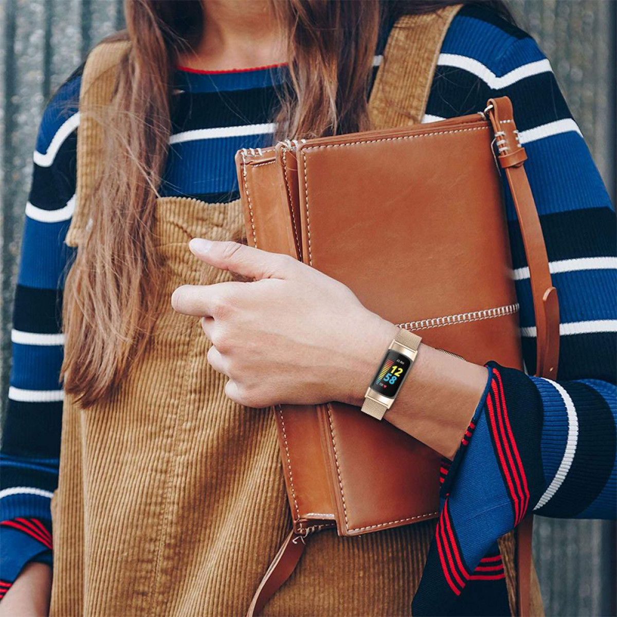 Frau mit goldener Uhr und Ledertasche. Die Uhr hat einen kleinen Bildschirm. Braune und blaue Kleidung.