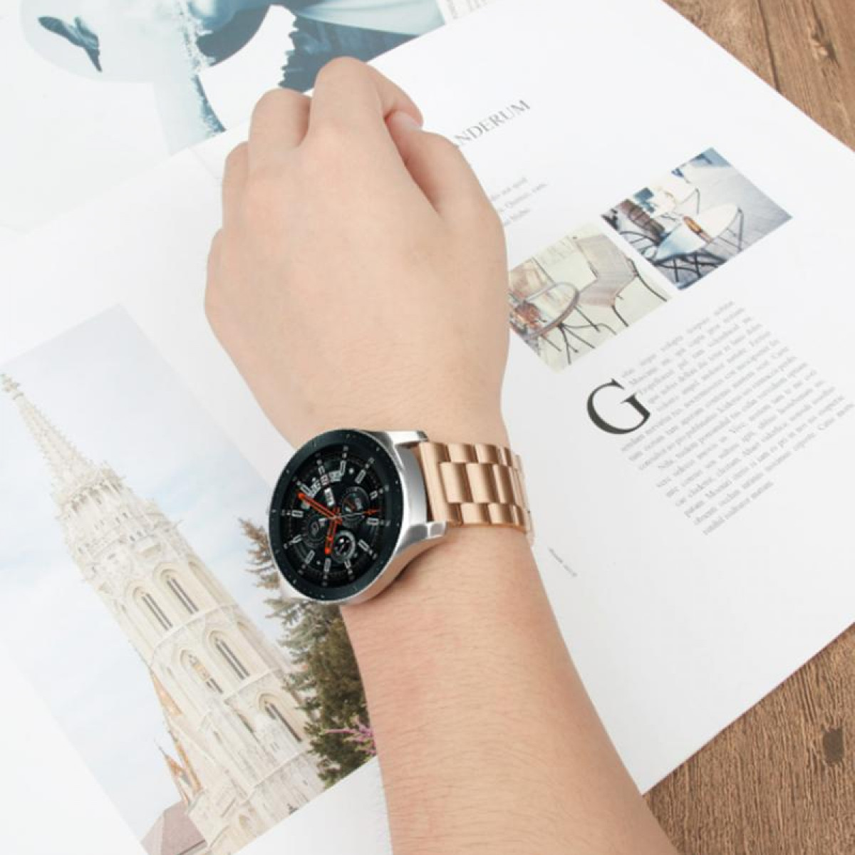 Eine Person, die eine roségoldene Smartwatch trägt und ein Papier mit architektonischen Zeichnungen hält.
