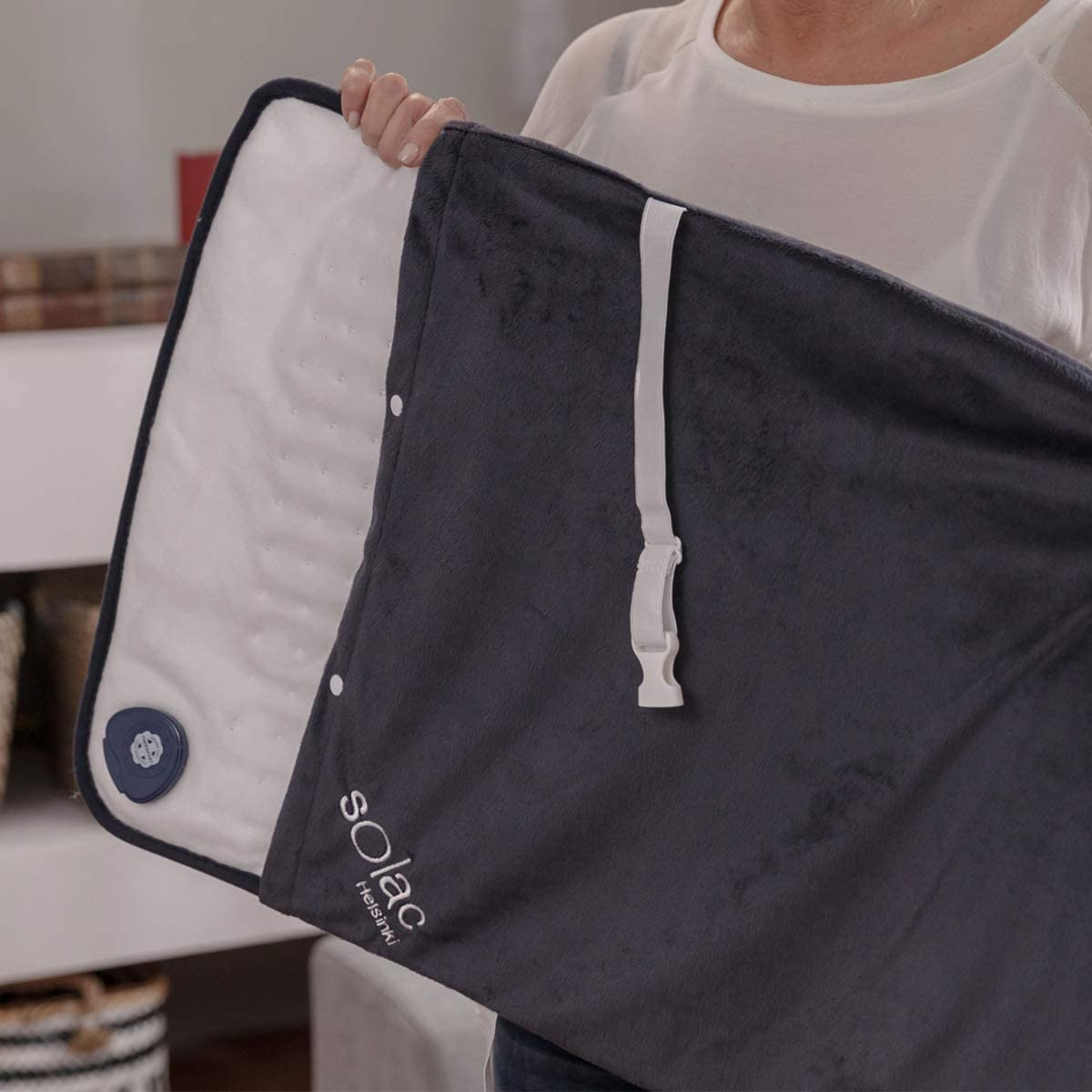 Osoba trzymająca otwarty koc grzewczy, ciemnoszara strona zewnętrzna i białe wnętrze.