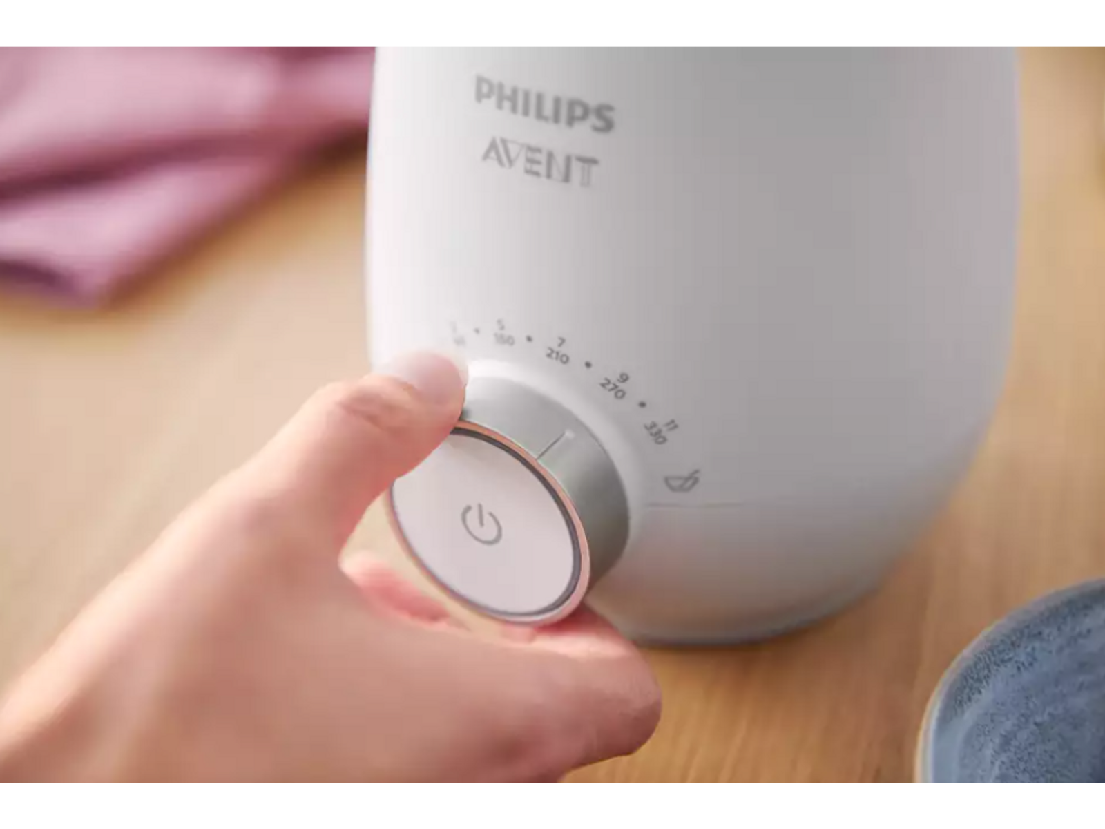 Una mano girando un dial en un calienta biberones Philips Avent blanco.