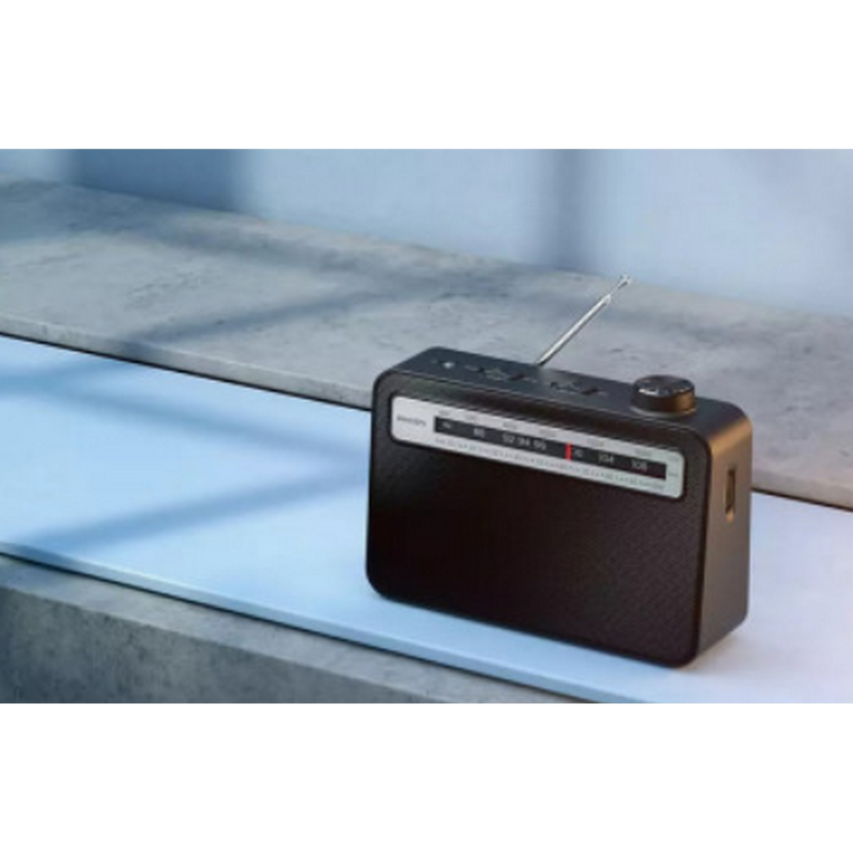 Czarne radio retro na niebieskiej powierzchni, ze srebrną anteną. Przód ma pokrętło.