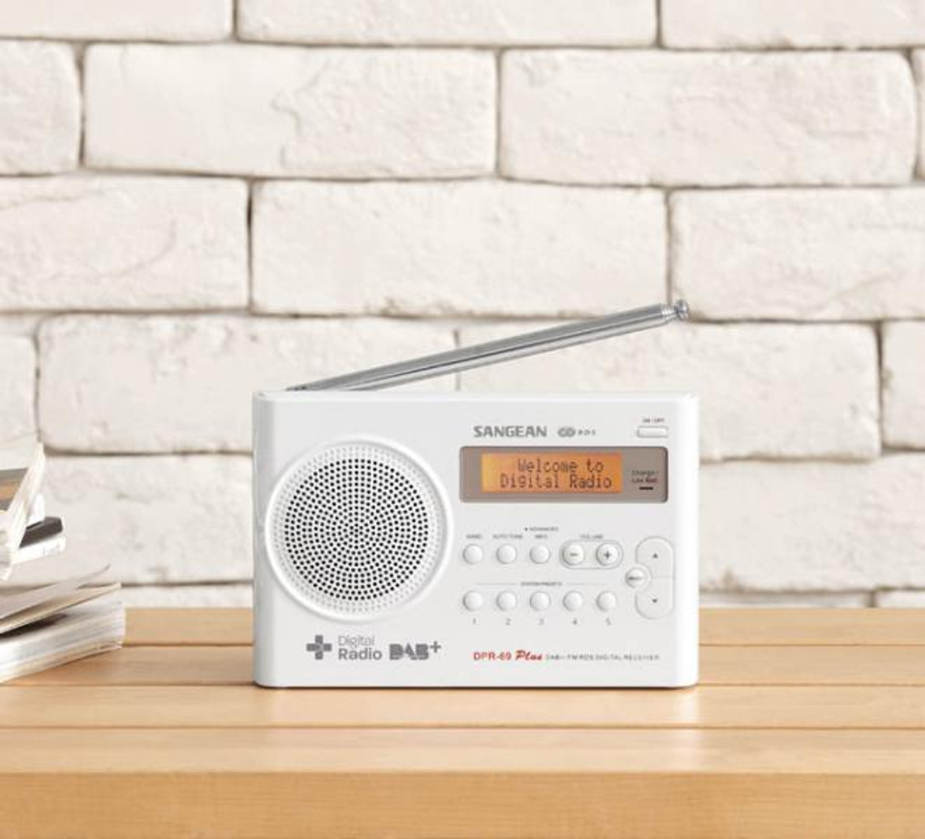 Weißes Digitalradio mit Lautsprecher, Display, Tasten und Teleskopantenne auf einem Holztisch.