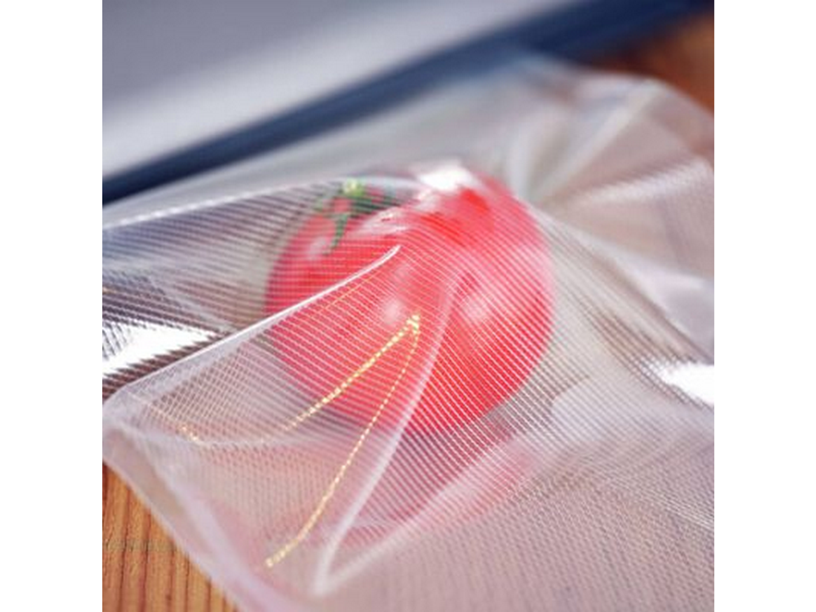 Un pomodoro rosso all'interno di un sacchetto trasparente sigillato sottovuoto, con rughe e riflessi di luce visibili.