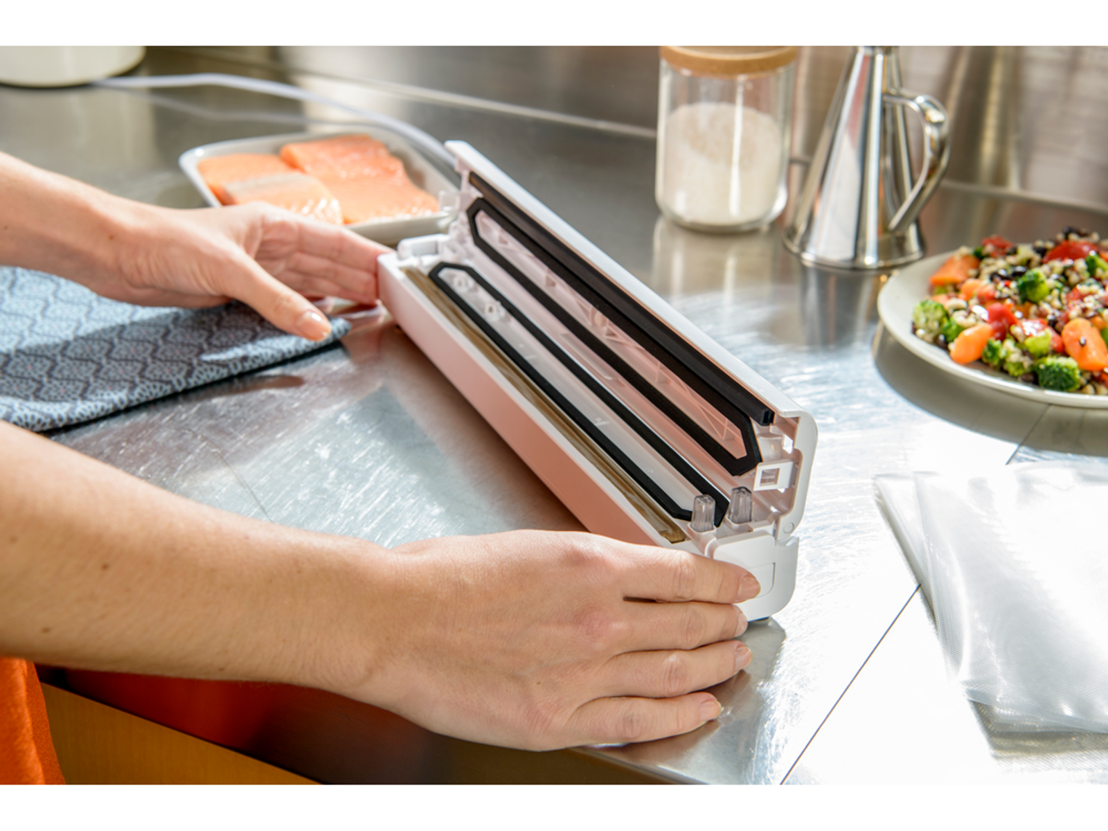 Ręce używające różowej zgrzewarki próżniowej do zgrzewania worka z żywnością, z składnikami.