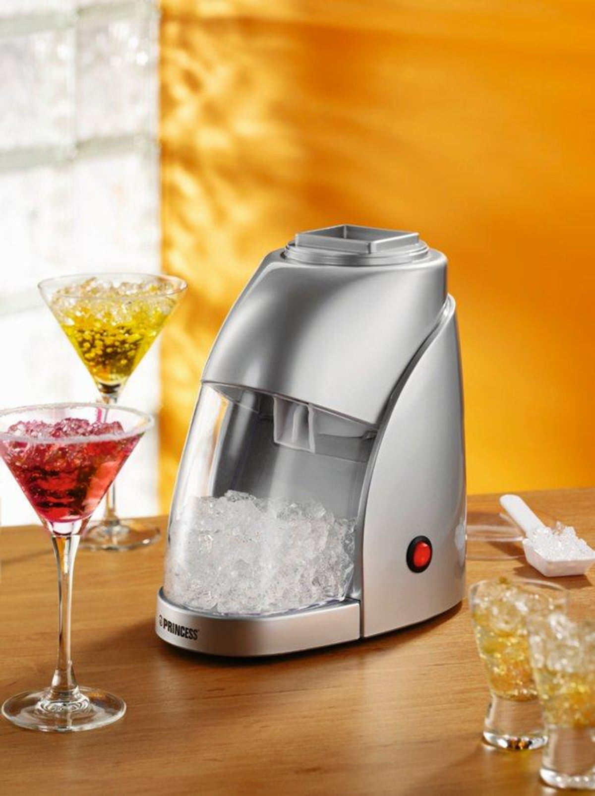 Silberne Eismaschine mit Eis. Zwei Cocktails und ein weißer Löffel daneben.