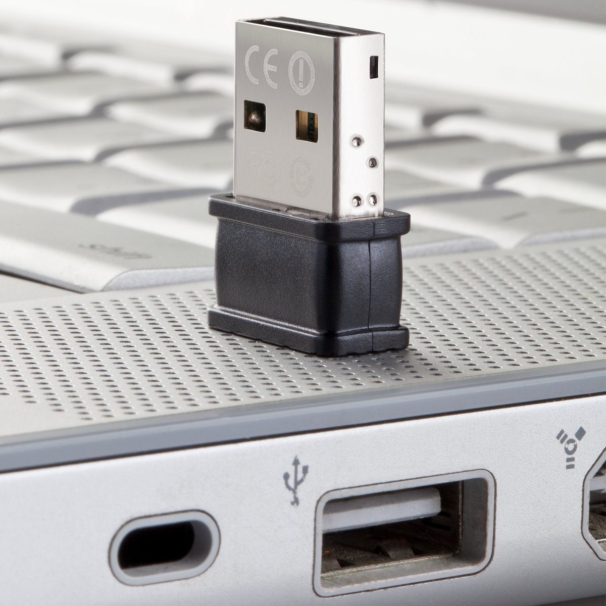 Adaptador USB plateado insertado en un adaptador negro, en un teclado plateado de portátil.