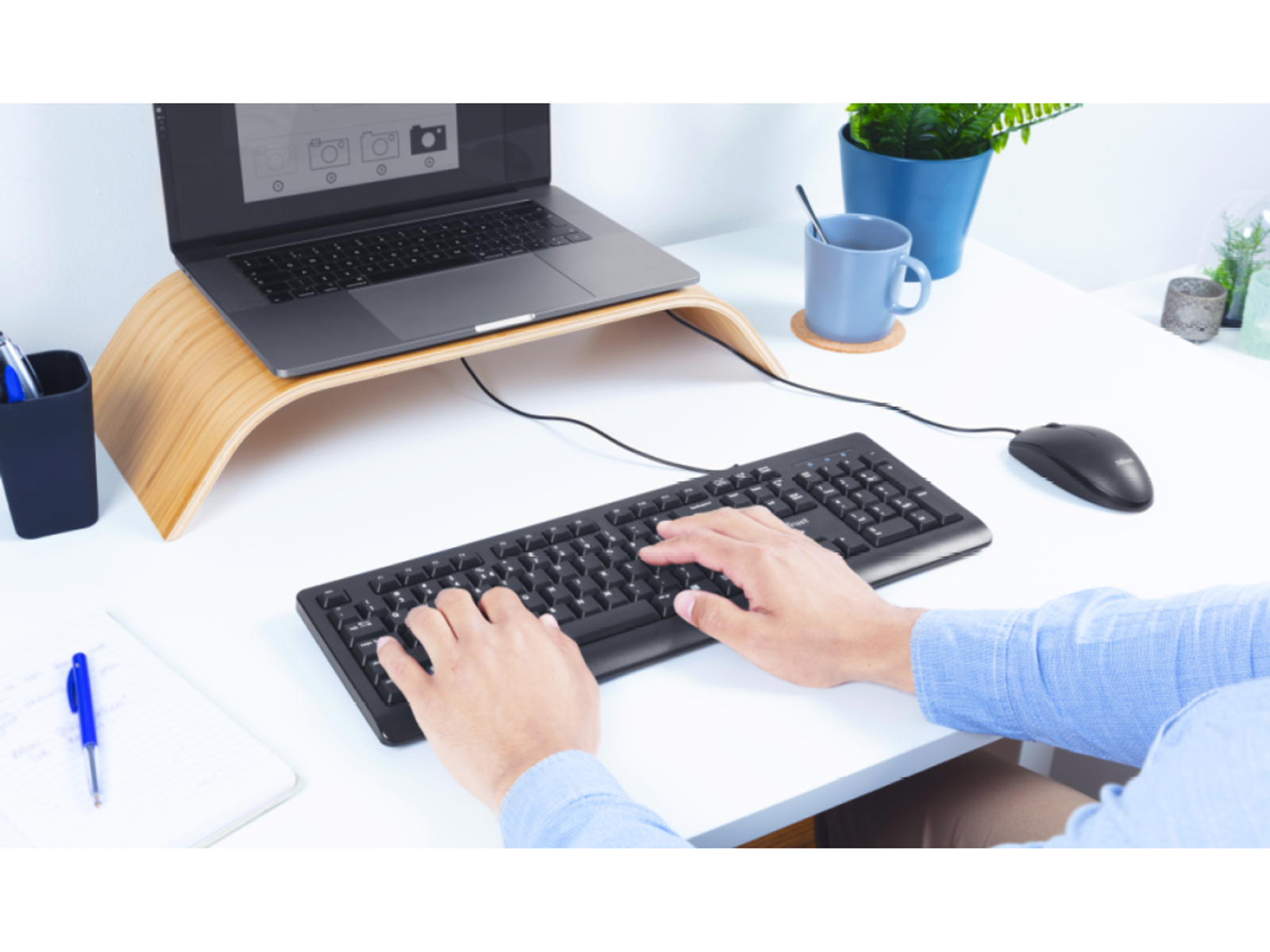 Ręce piszące na czarnej klawiaturze. Laptop na drewnianym stojaku. Czarna mysz na biurku.