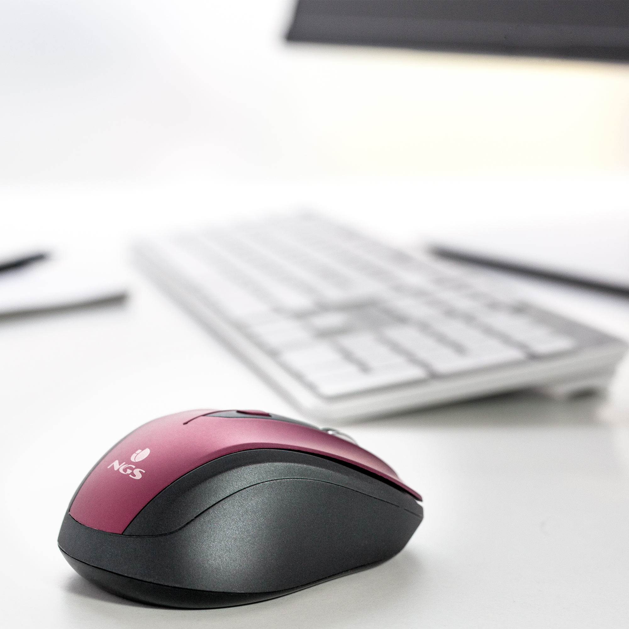 Rote und schwarze Maus auf einem weißen Schreibtisch, mit einer Tastatur dahinter.