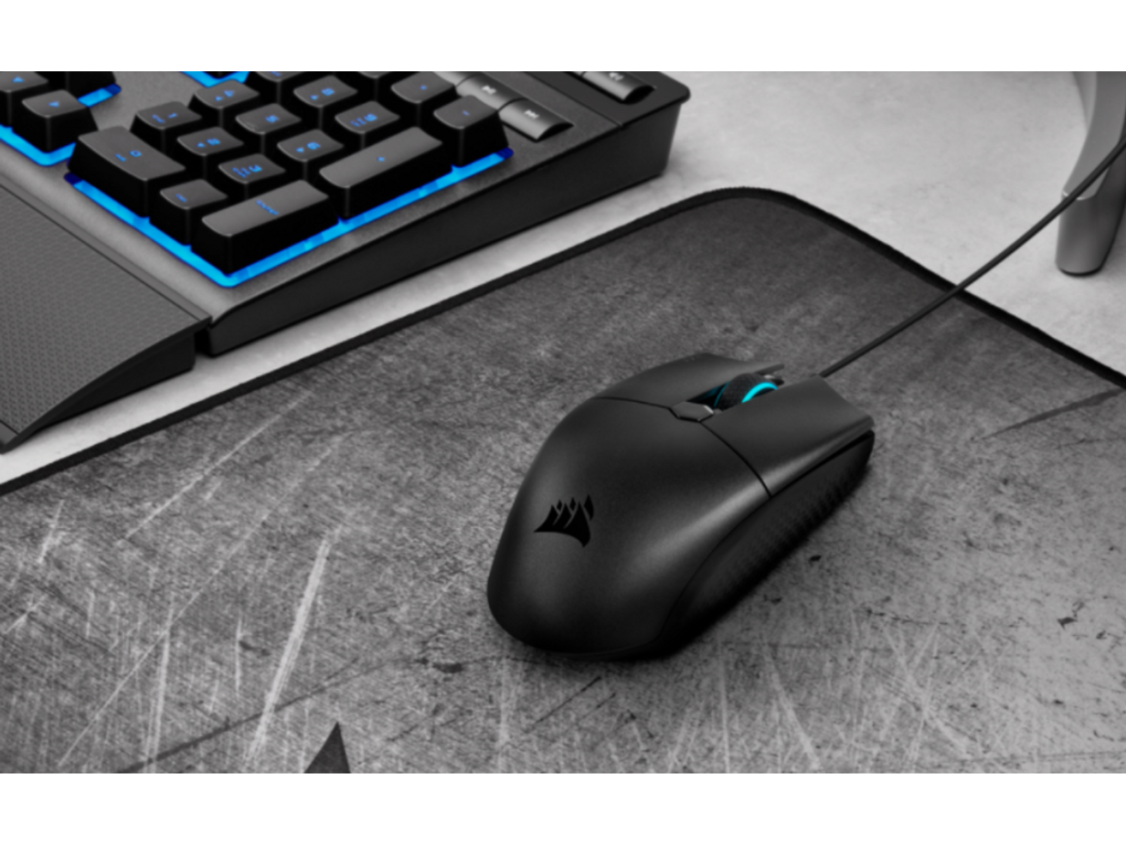 Czarna mysz do gier na podkładce, z klawiaturą w tle. Mysz ma niebieskie światła.