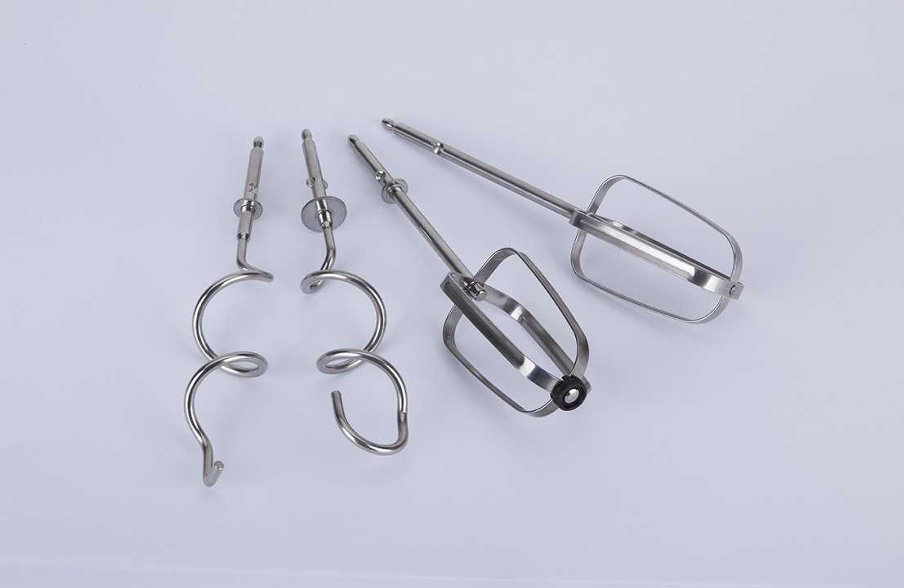 Varios accesorios metálicos para batidora. Dos ganchos en espiral y dos batidores planos. Fondo blanco.