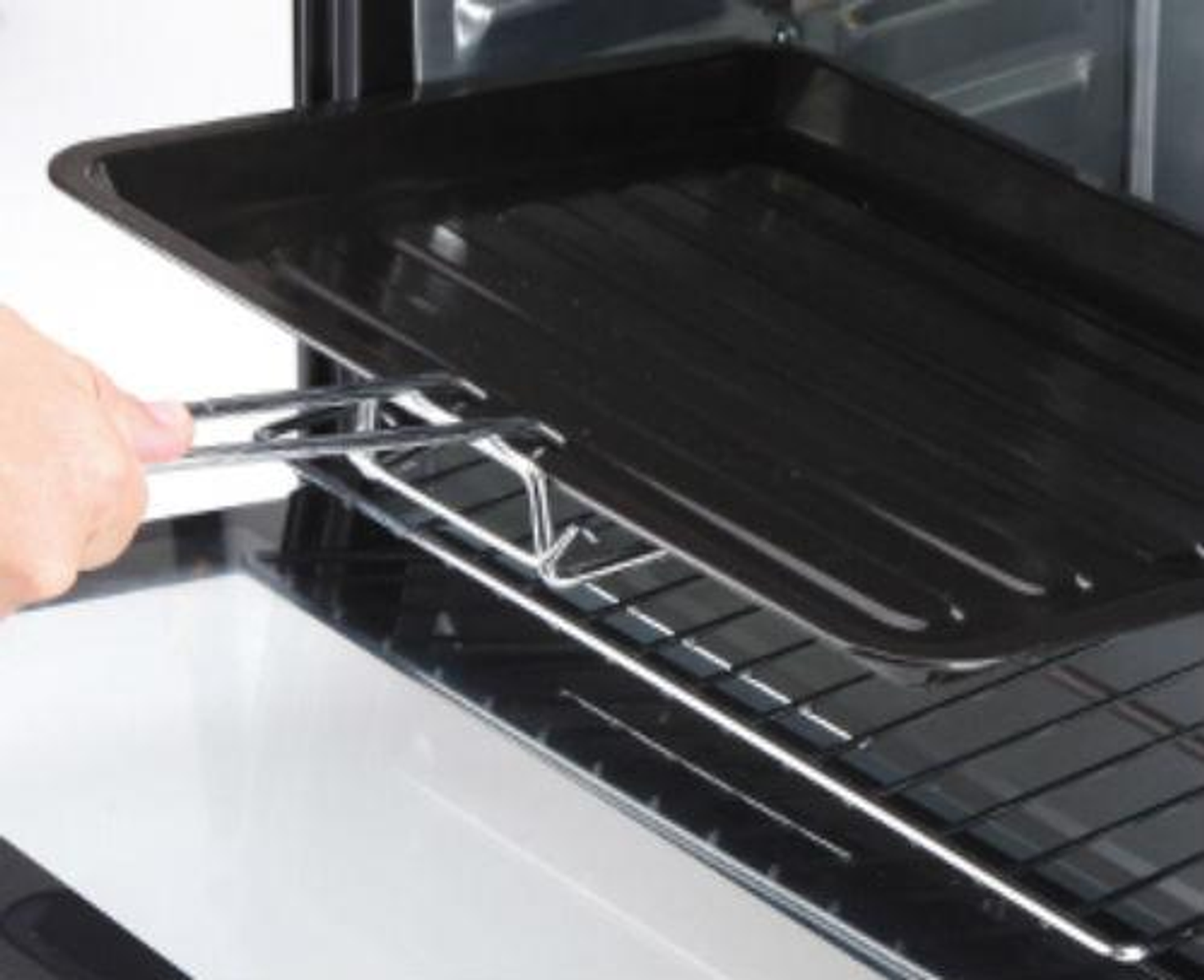 Zbliżenie czarnego piekarnika, osoba wyciąga tacę za pomocą szczypiec. Taca jest czarna.