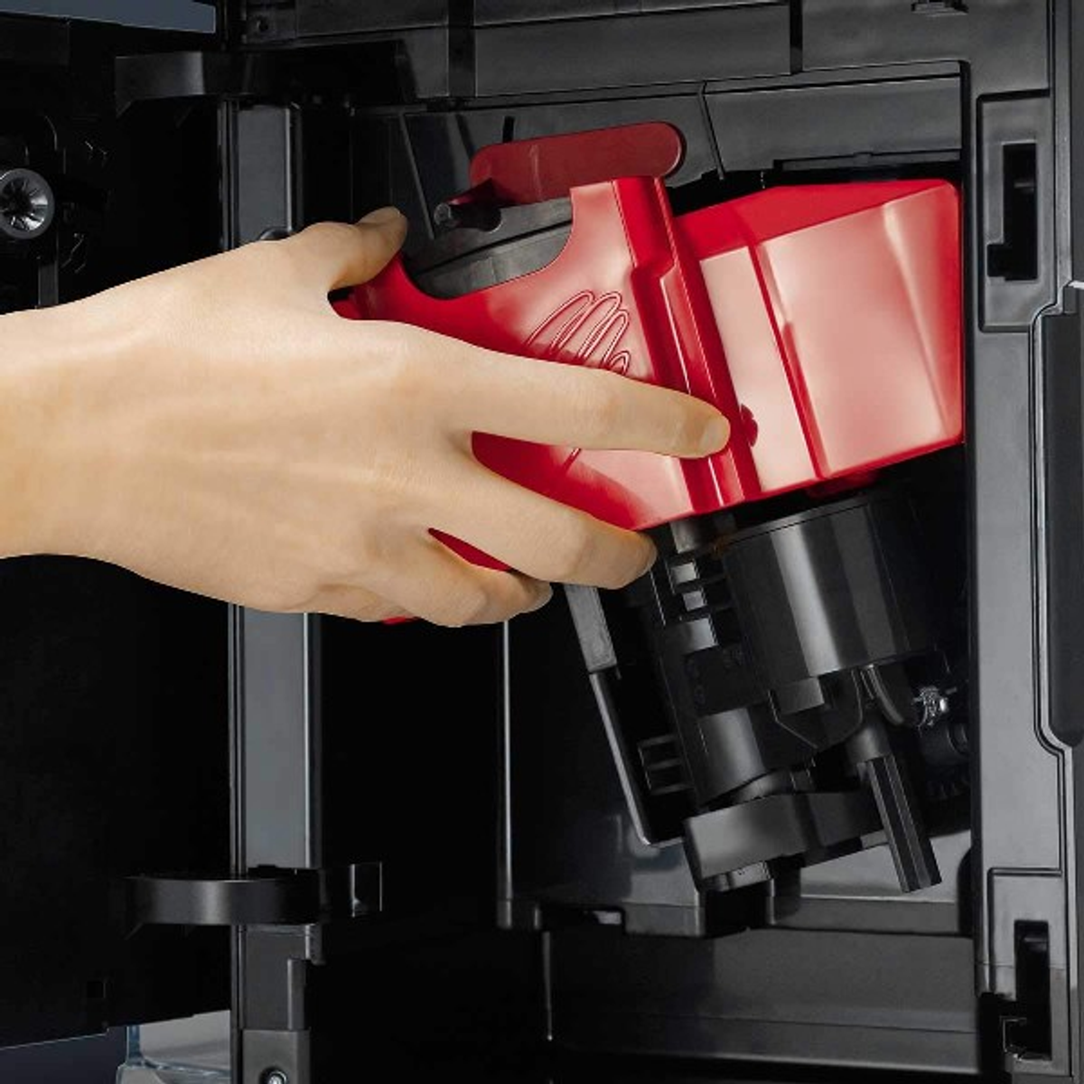 A hand holding a red part of a coffee machine, over the machine.