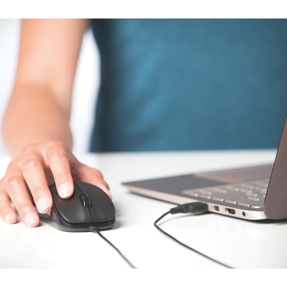 Una persona usa un ratón negro conectado a una computadora portátil en un escritorio blanco.
