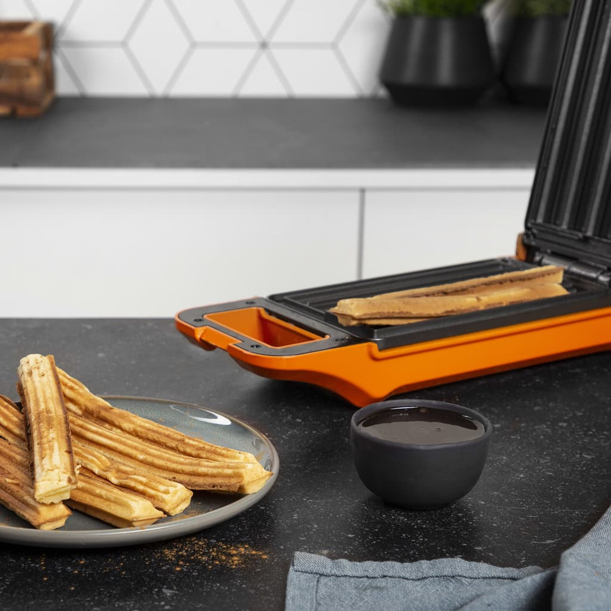Una macchina per churros arancione con churros e un piatto di cioccolato. Primo piano.
