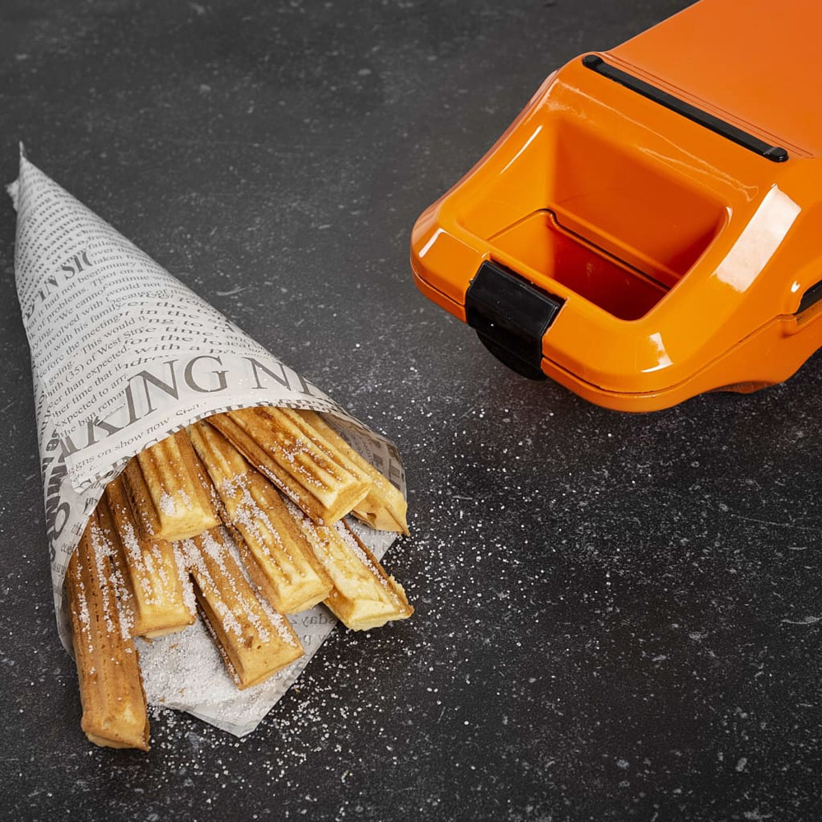 Churros in un cono di carta, con zucchero. Una piastra per waffle arancione sullo sfondo.