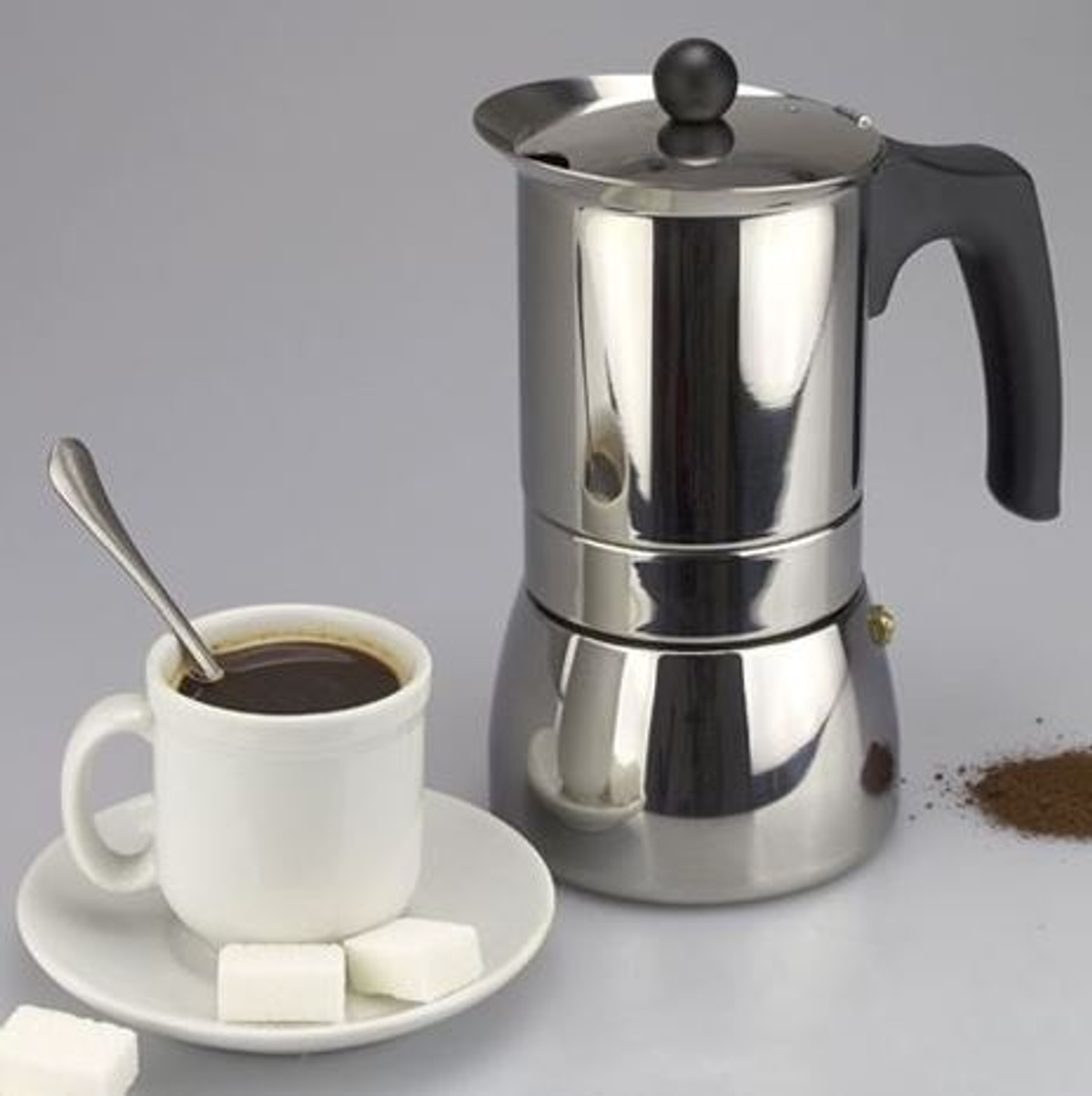 Cafetera de acero inoxidable con taza de café, platillo, terrones de azúcar y café molido.