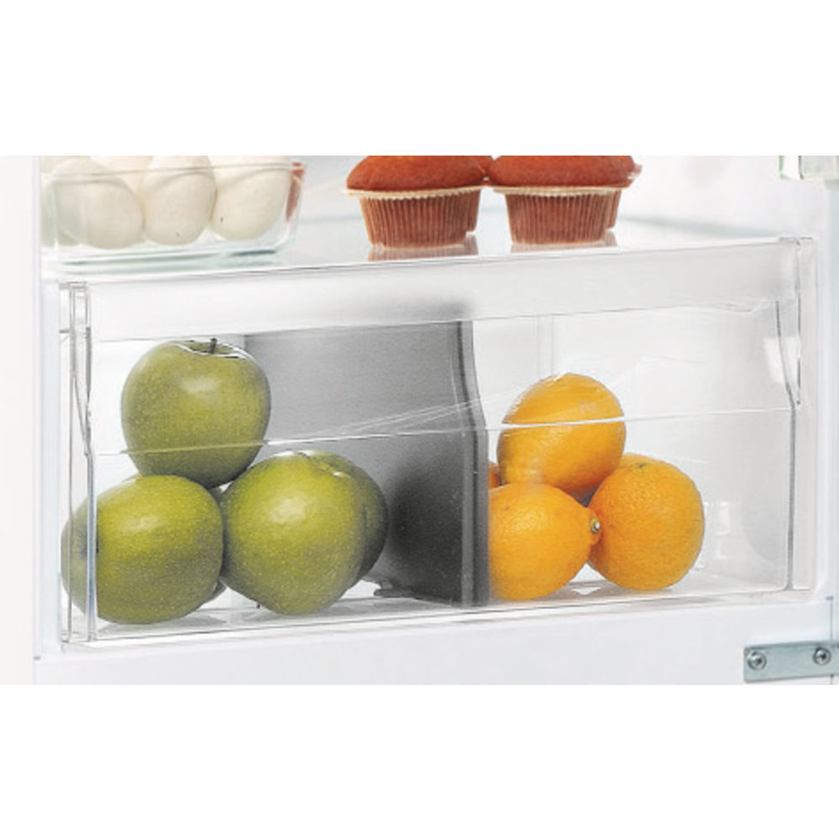 Cassetto trasparente del frigorifero con mele verdi, limoni e muffin.