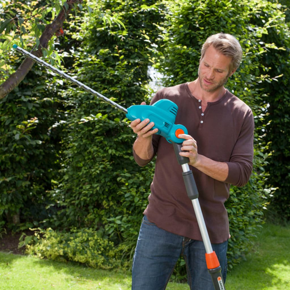 Mann, der eine Heckenschere benutzt, um einen Ast in einer grünen Gartenumgebung an einem sonnigen Tag zu schneiden.