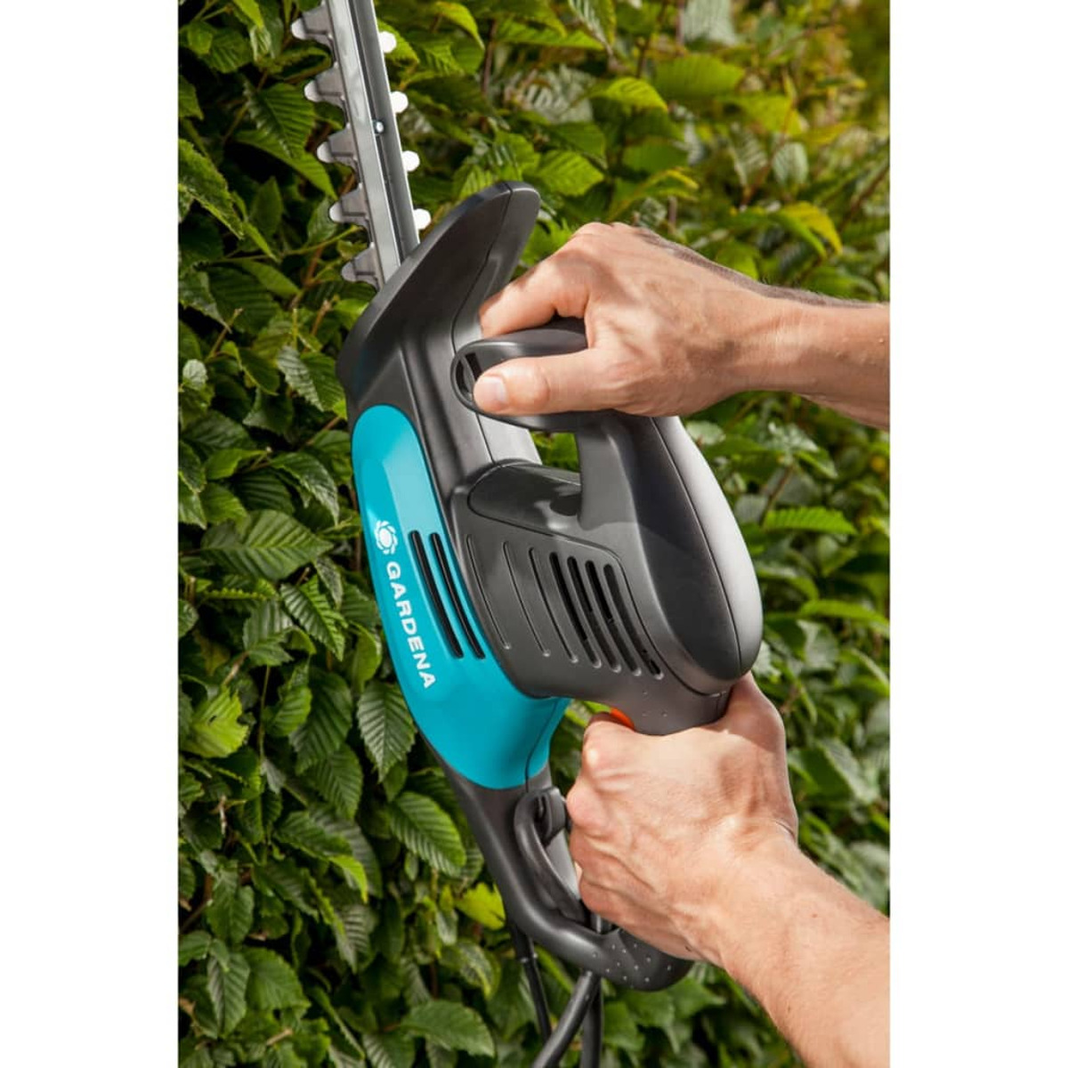 Tagliasiepi Gardena in uso. Turchese e nero con mani che lo tengono.