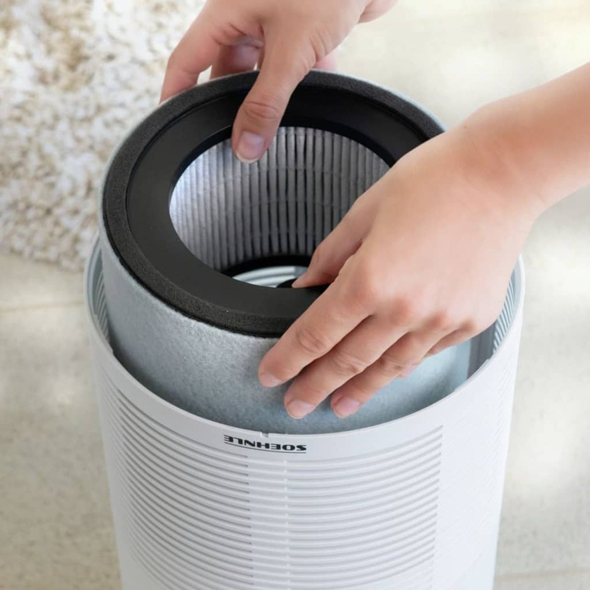 Hände, die einen weißen Luftfilter in einen weißen Luftreiniger halten und installieren.