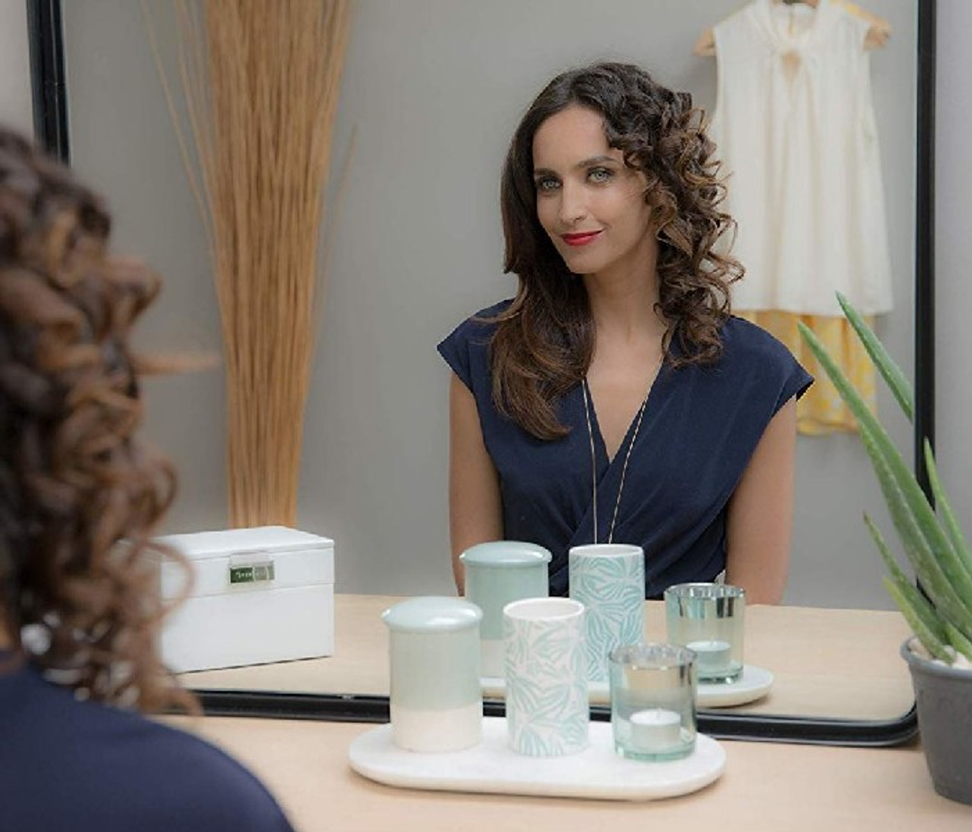 Kobieta patrząca w lustro z dekoracjami. Obecne jest białe pudełko i rośliny.