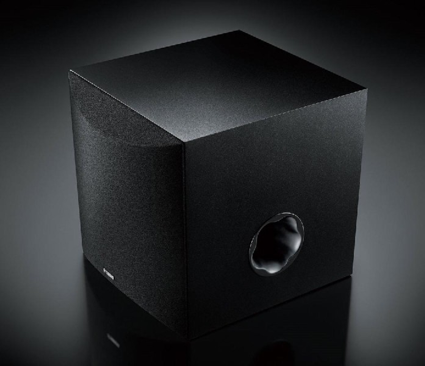 Subwoofer negro con puerto redondo. Está sobre una superficie negra.