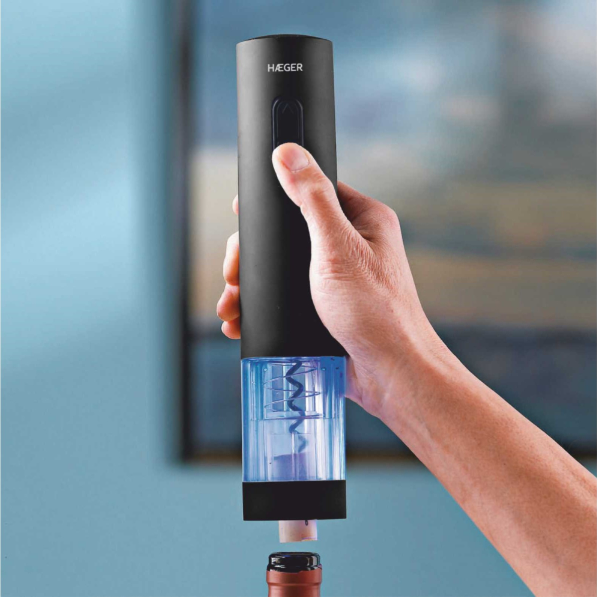 Sacacorchos eléctrico negro sacando un corcho de una botella de vino. Fondo azul.