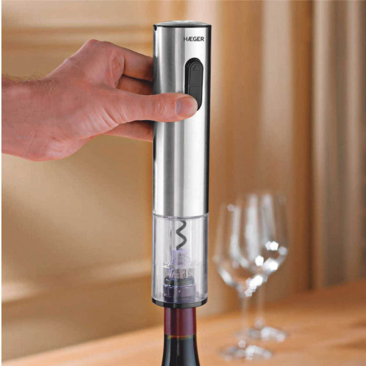 Un abridor de vino eléctrico plateado con una botella de vino. Una mano está operando el abridor.