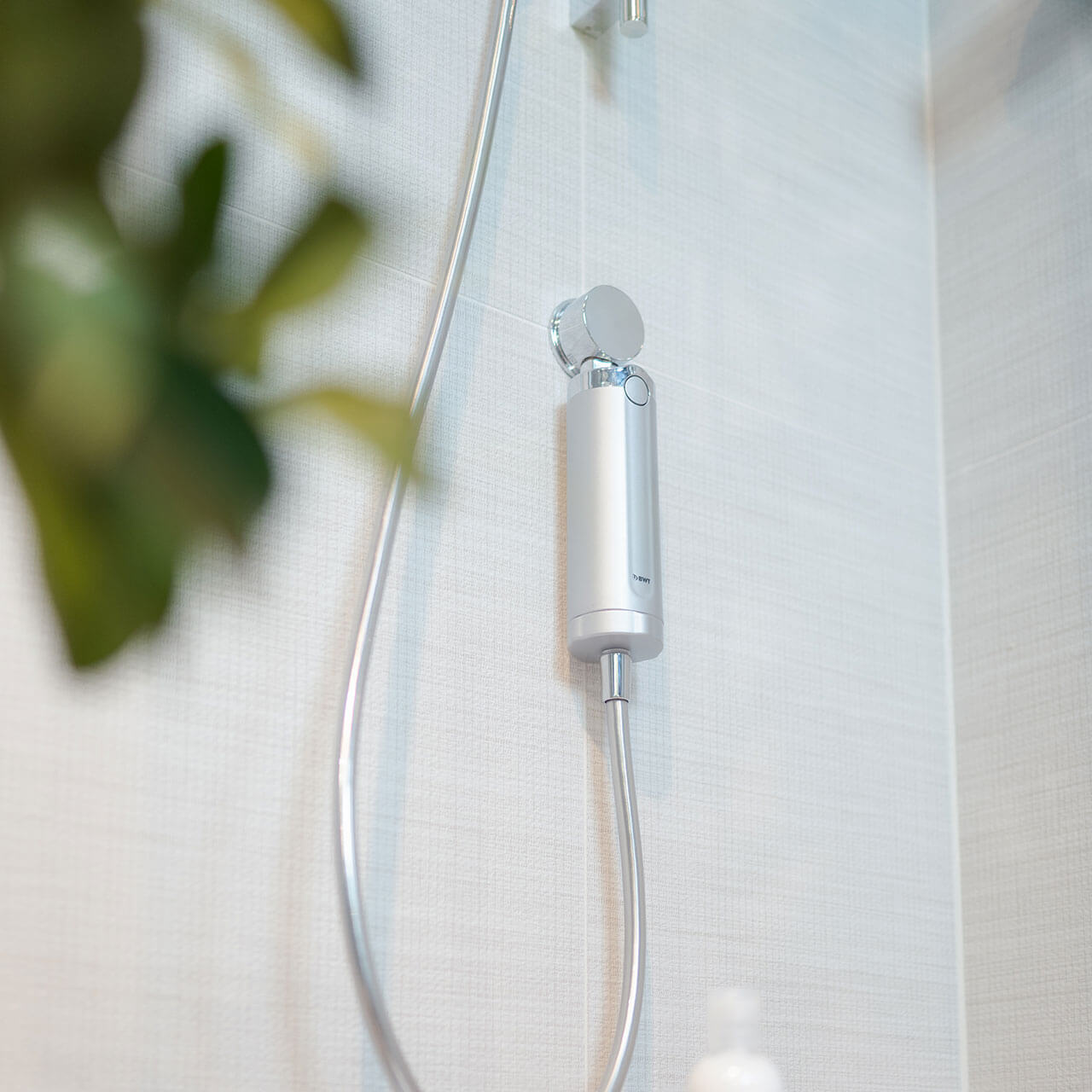 Chromowana głowica prysznicowa i wąż w łazience, z kafelkami.