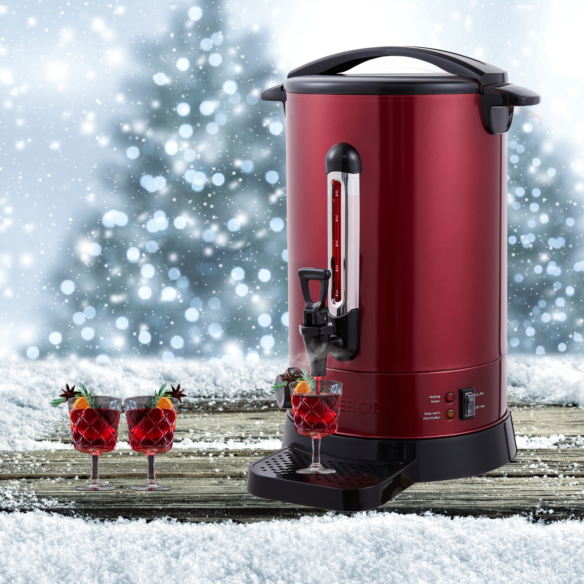 Roter Getränkespender auf einem Holztisch mit Gläsern. Verschneiter Hintergrund und Weihnachtslichter.
