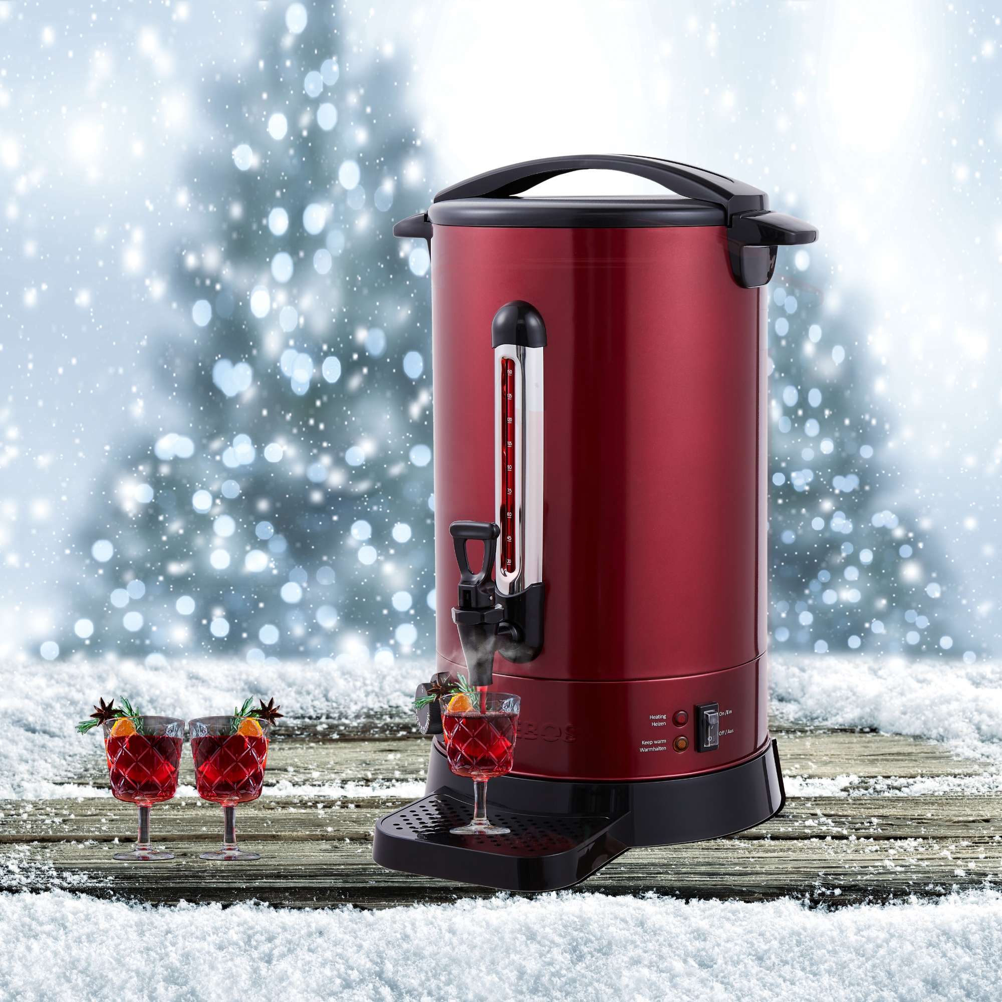 Roter Getränkespender mit Gläsern. Schnee und verschwommener Weihnachtsbaumhintergrund.