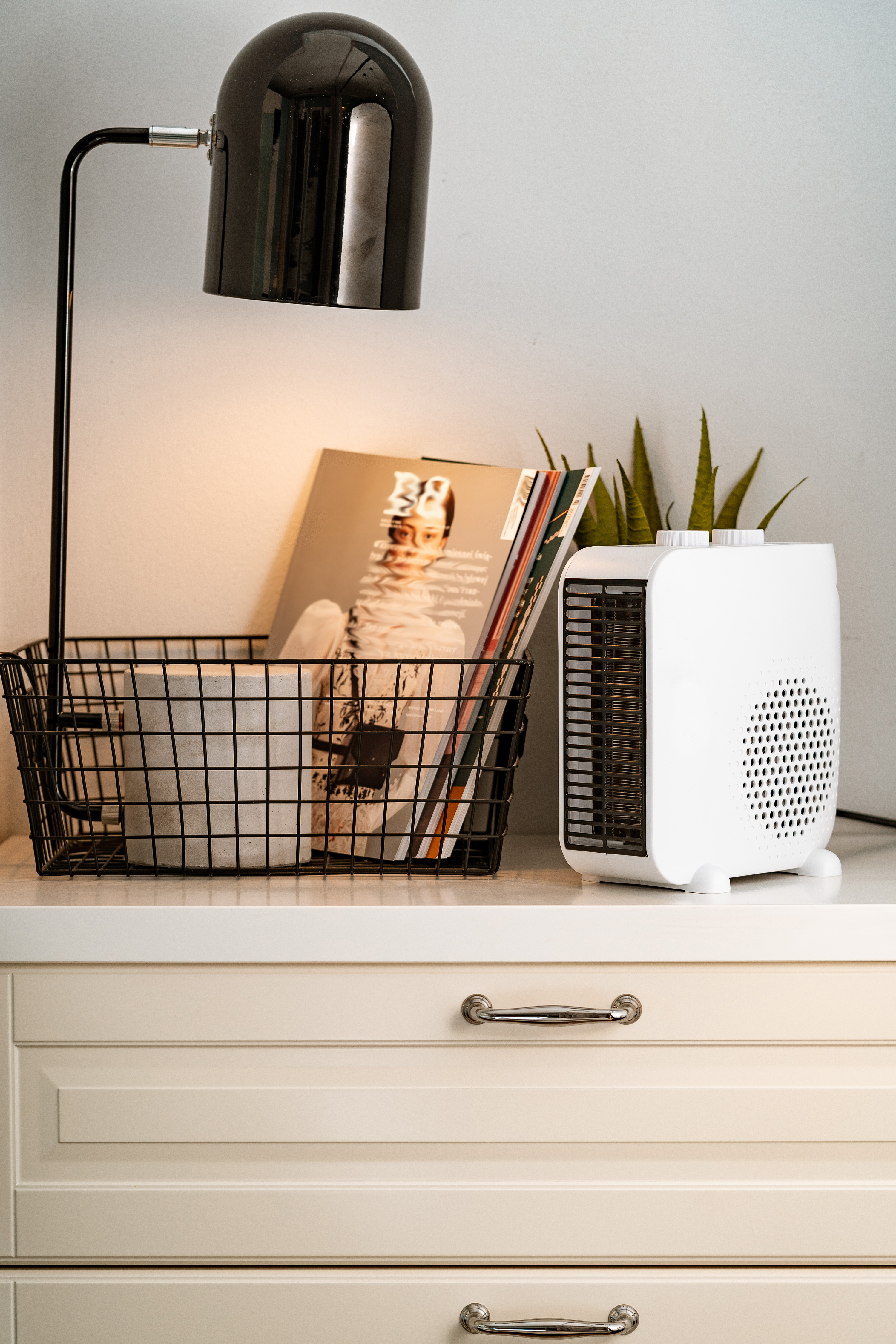 Biała komoda z lampą, czasopismami i białym grzejnikiem. Czarna lampa znajduje się na górze.