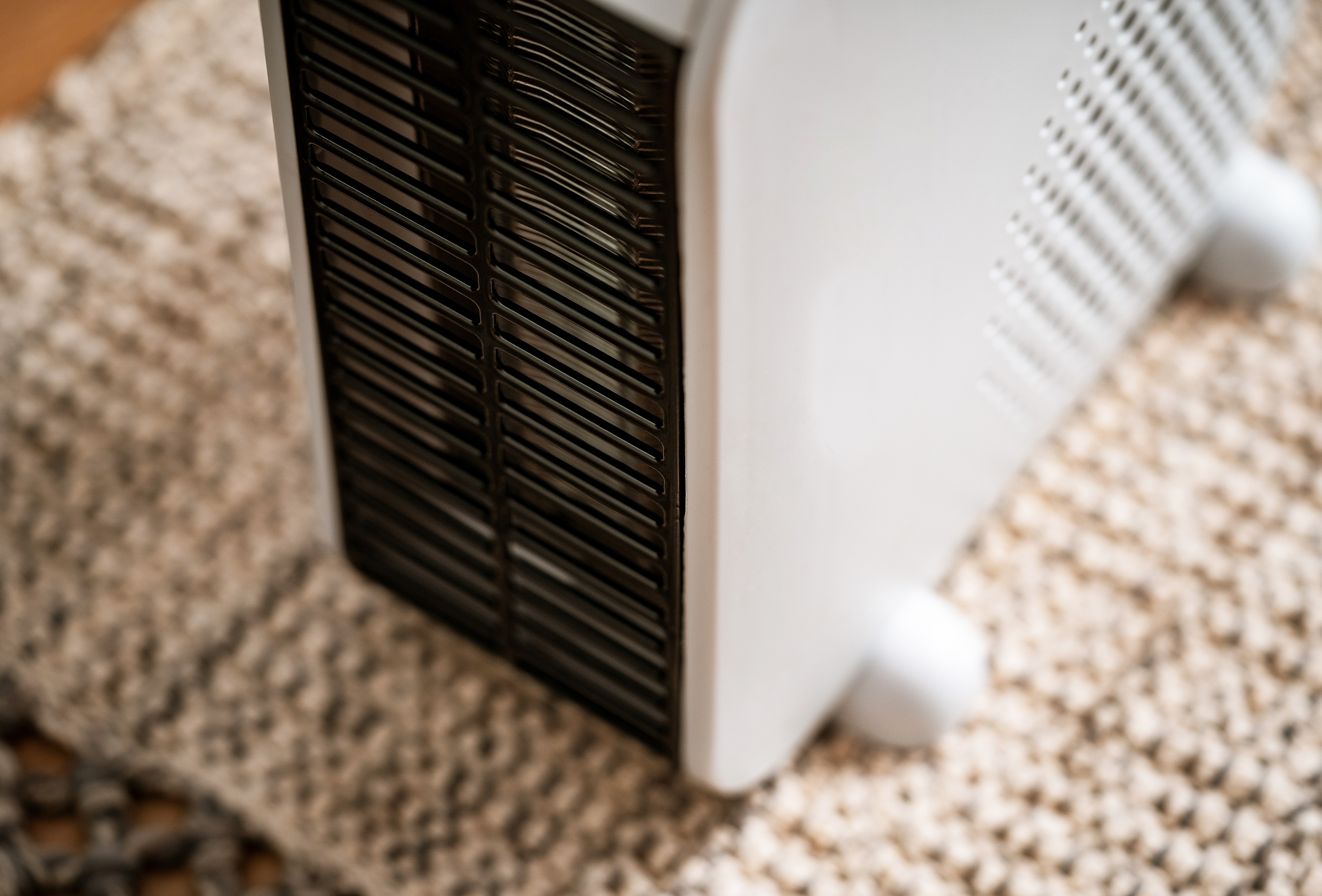 Biały grzejnik elektryczny z czarną kratką, umieszczony na teksturowanym dywanie.