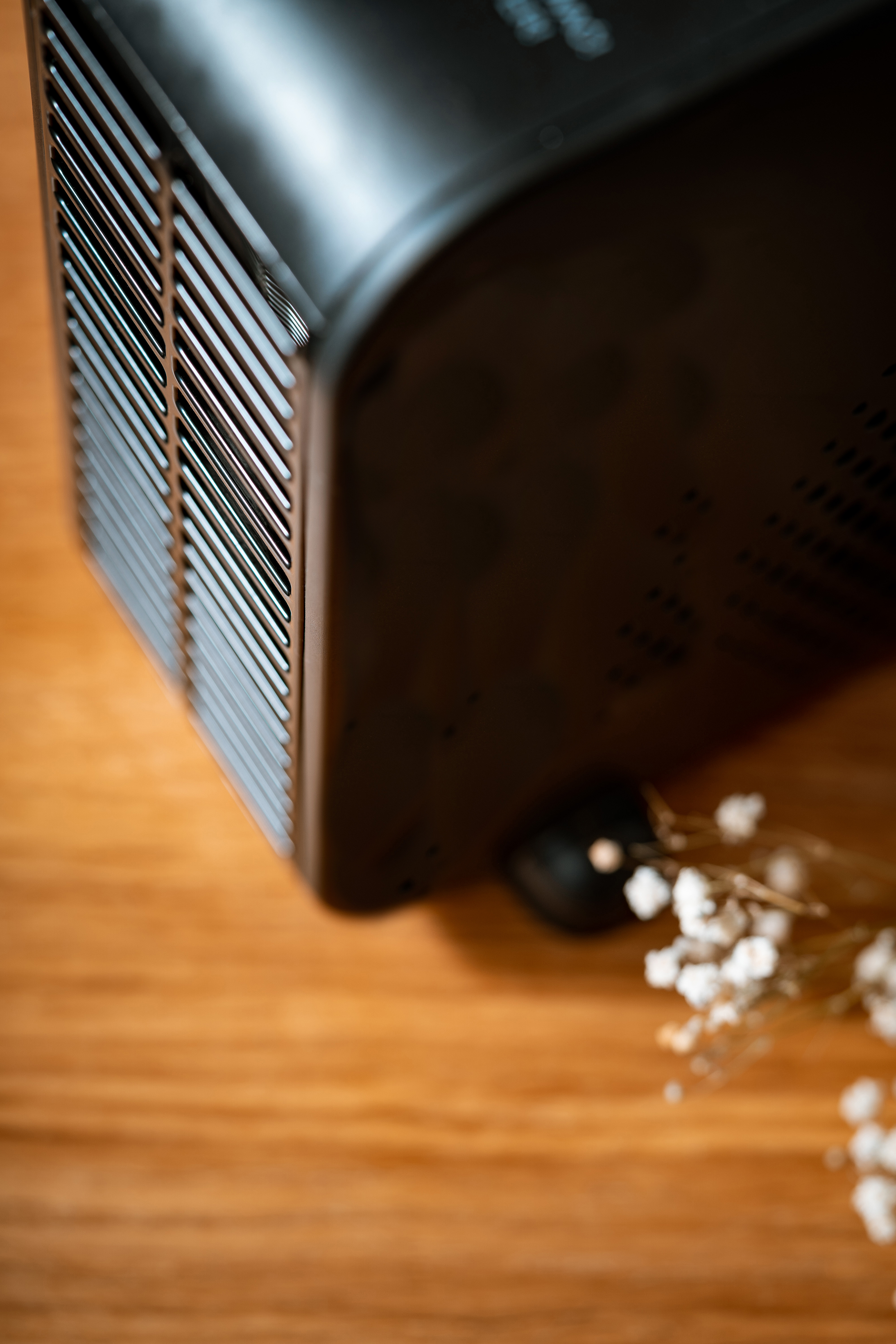 Zbliżenie czarnego urządzenia z metalową kratką i małą czarną kulką na drewnianej powierzchni.