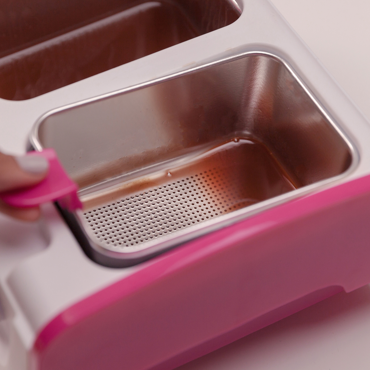 Aparato de limpieza rosa y blanco con un recipiente interno de acero inoxidable que contiene líquido.