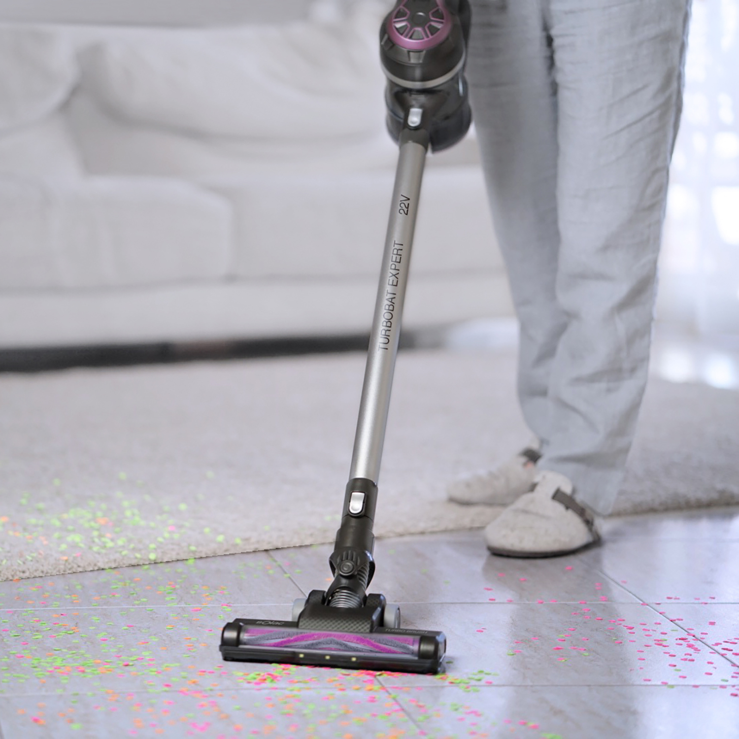 Persona aspirando una habitación con una aspiradora inalámbrica. Confeti en el suelo.