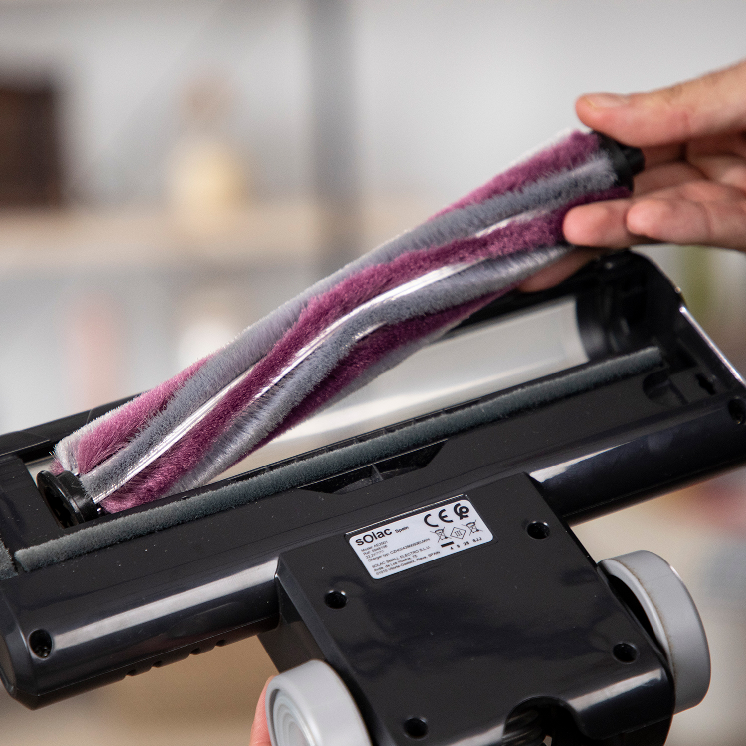 Primer plano del cepillo de una aspiradora con un rodillo morado y gris dentro del cabezal de limpieza.