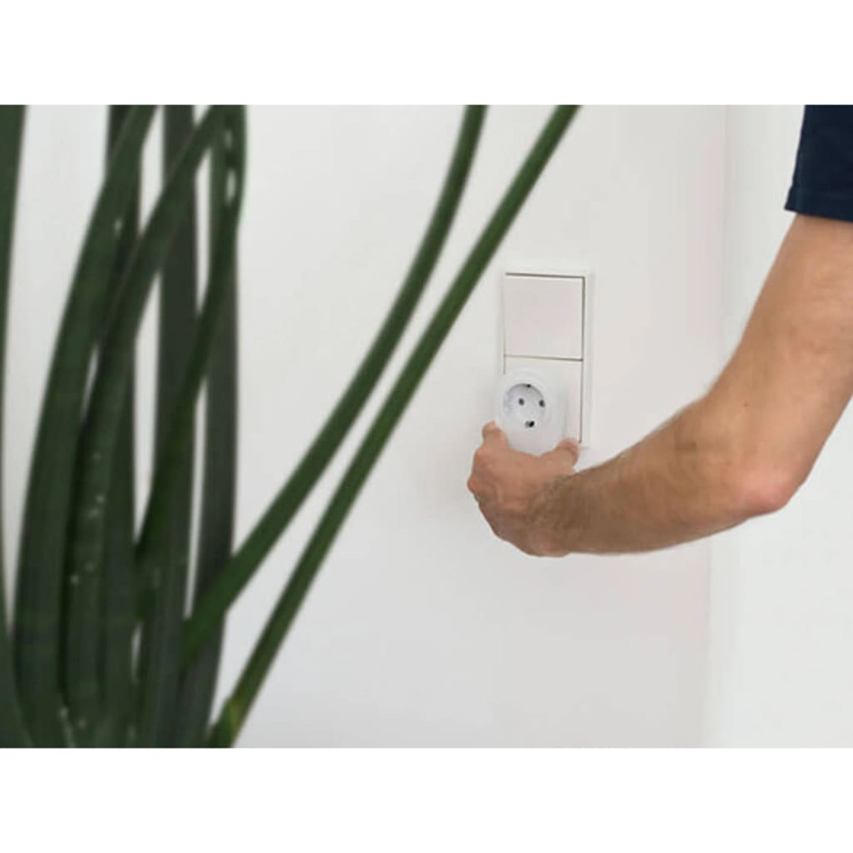 Eine Hand steckt einen weißen Stecker in eine weiße Steckdose.