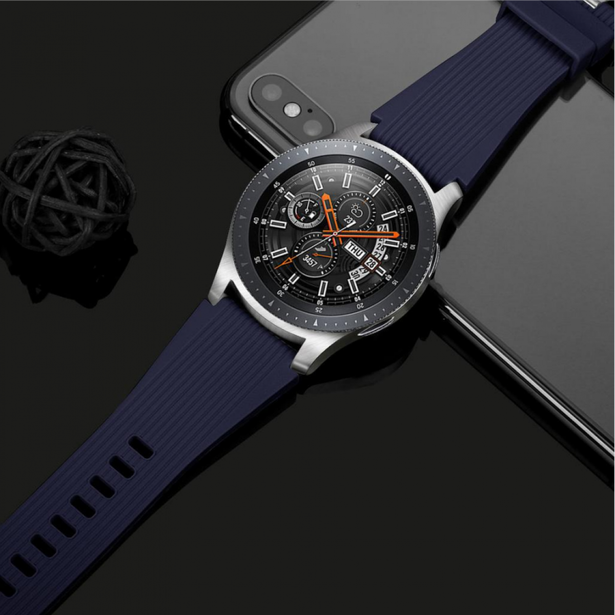 Eine silberne Smartwatch mit dunkelblauem Armband auf schwarzer Oberfläche neben einem Telefon.